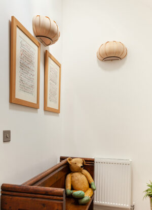 Handmade baby pumpkin wall lights in a hall way above picture frames and a wooden seat.