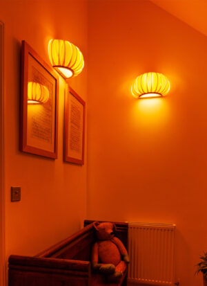 Handmade baby pumpkin wall lights glowing above pictures and a wooden seat.
